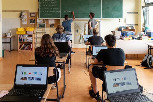 Schüler*innen in einer Schulklasse, die jeder einen Laptop vor sich stehen haben.
